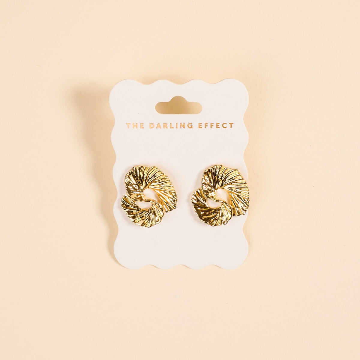 The Ripple Effect Standout Earrings by The Darling Effect feature a textured heart design and are displayed on a white card with brand text, set against a cream background—stylish statement jewelry for any occasion.