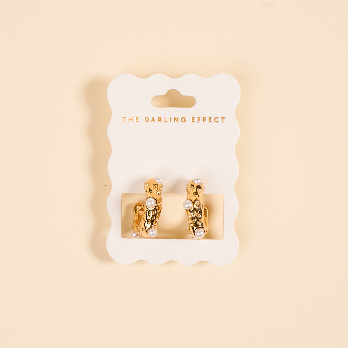 The Darling Effect’s Say It All Standout Earrings feature a golden, high-shine textured design with small white pearls, showcased on a white scalloped card labeled "The Darling Effect" against a light beige background.