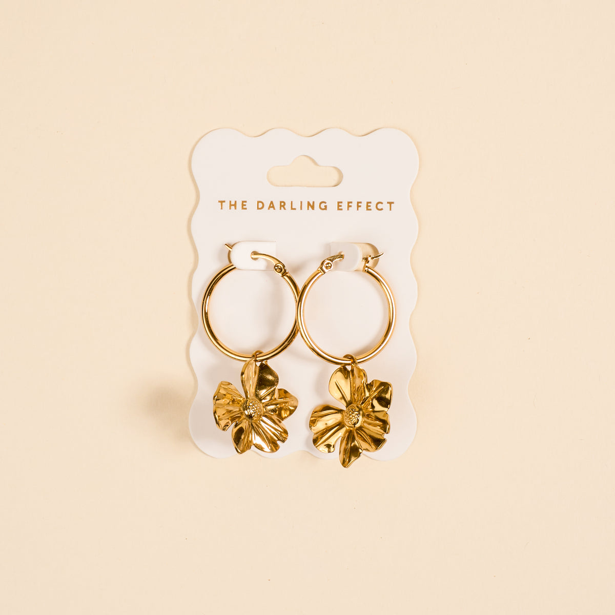 Sunlit Petal Standout Earrings by The Darling Effect feature high-shine golden finish and dangling flower charms, displayed on a white card—perfect for special occasions against a soft beige background.