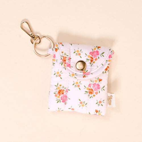 The-darling-effect’s Endless Daydream Cream Puffy Earbud Case Keychain features a quilted white design with pink and orange floral print, a gold snap closure, and a matching gold earbud keychain.