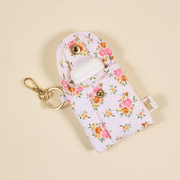 The Endless Daydream Cream Puffy Earbud Case Keychain by the-darling-effect is open, displaying white wireless earbuds inside. Its floral design and gold keychain clip stand out against a beige background.