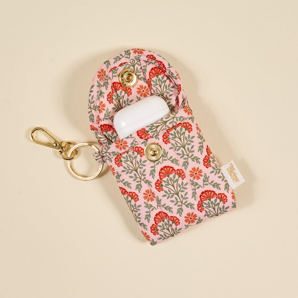 The Darling Effect Everbloom Dusty Rose Puffy Earbud Case, featuring a floral design and gold snap closure, is displayed on a beige background—ideal for carrying your wireless earbuds in style every day.