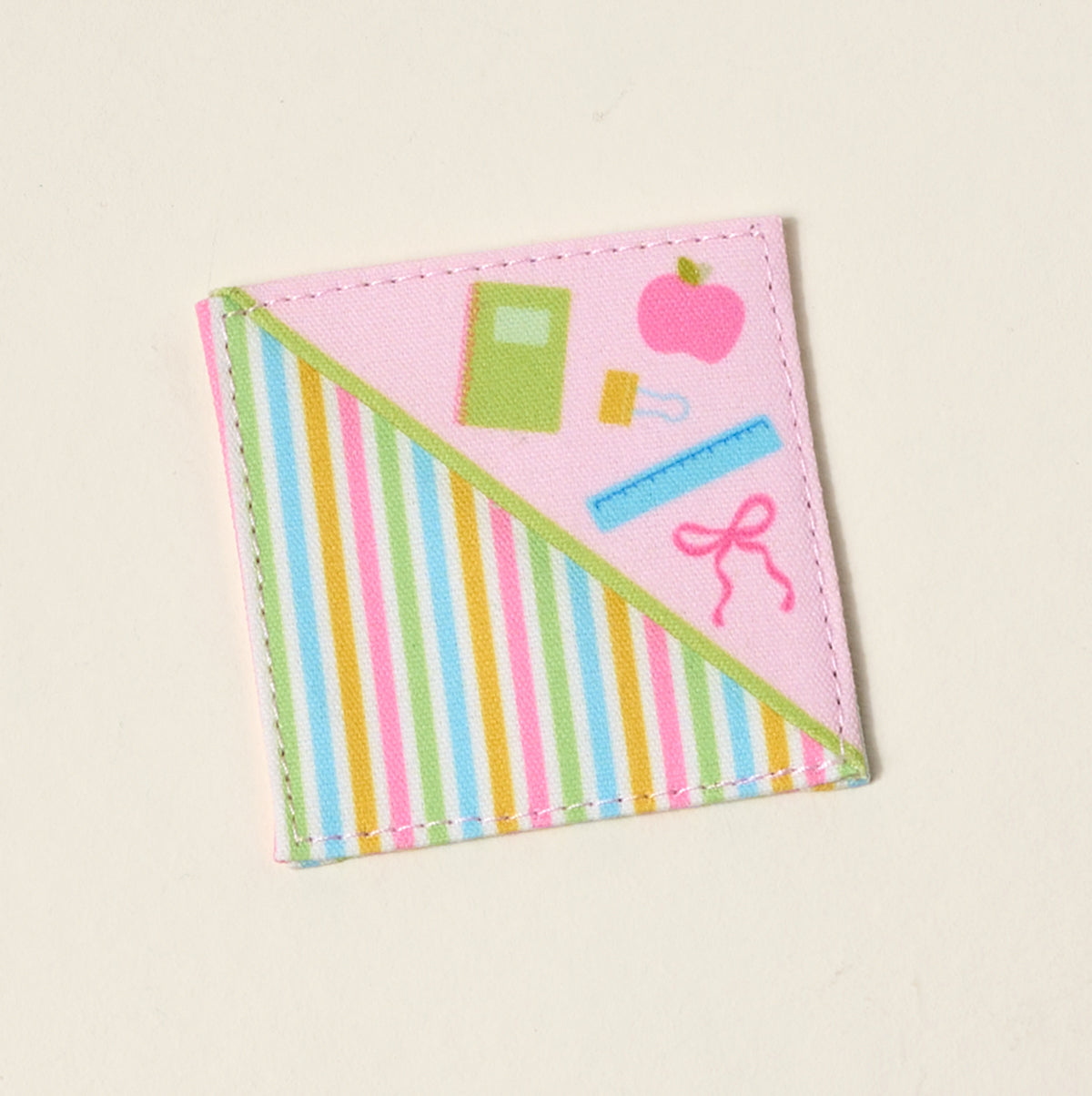The Darling Effect’s Color Me Happy Corner Keeper Fabric Bookmark features pink fabric with school-themed illustrations and colorful diagonal stripes—a fun, thoughtful gift for book lovers.