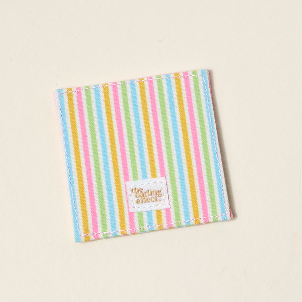 The Color Me Happy Corner Keeper Fabric Bookmark by The Darling Effect features vertical pastel stripes and a white label with gold lettering—an adorable, square corner bookmark and a perfect gift for book lovers.