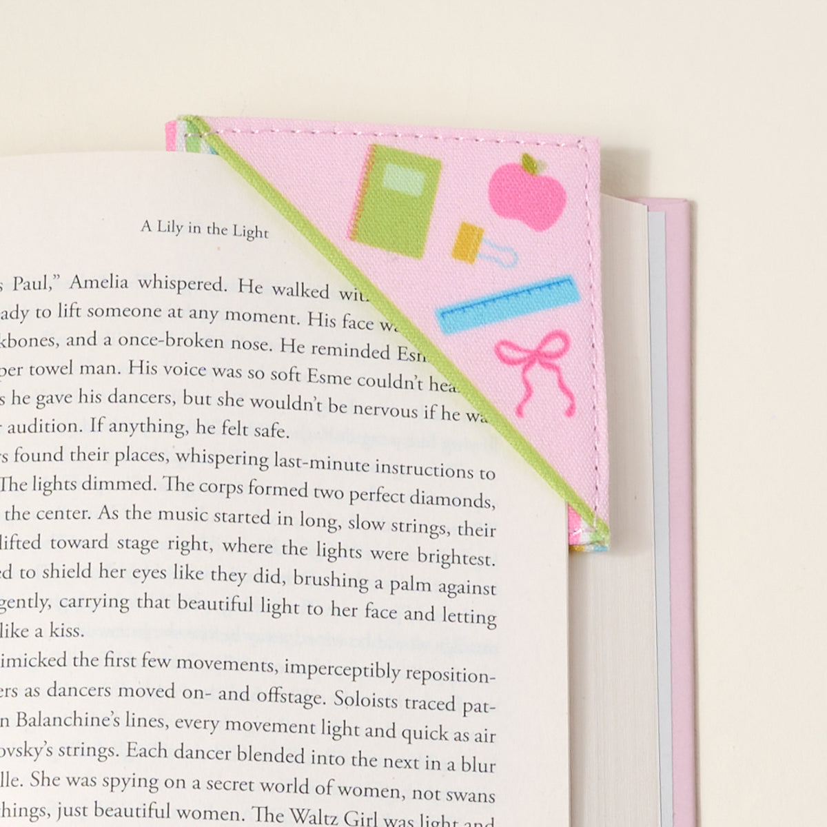 The Darling Effect’s Color Me Happy Corner Keeper Fabric Bookmark features pastel tones and simple art of a green book, pink pencil, and ribbon—resting on your page for the perfect book lover gift.