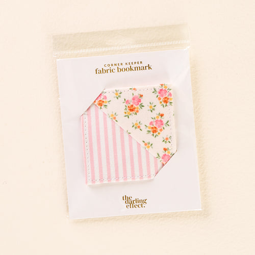 The Endless Daydream Cream Corner Keeper Fabric Bookmark by the-darling-effect features pink stripes and a floral pattern, packaged in a clear sleeve with a "CORNER KEEPER fabric bookmark" label—an ideal gift for book lovers.