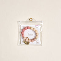 The-darling-effect’s Mauve Muse Hands-Free Keychain Wristlet, featuring pink and beige silicone beads with gold accents, is shown in a clear pouch with a gold grommet against a light beige background.