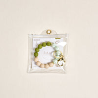 The Darling Effect’s Olive Branch Hands-Free Keychain Wristlet features green, white, and beige silicone beads with a gold keyring, packaged in a clear snap pouch and includes a branded card for extra style.