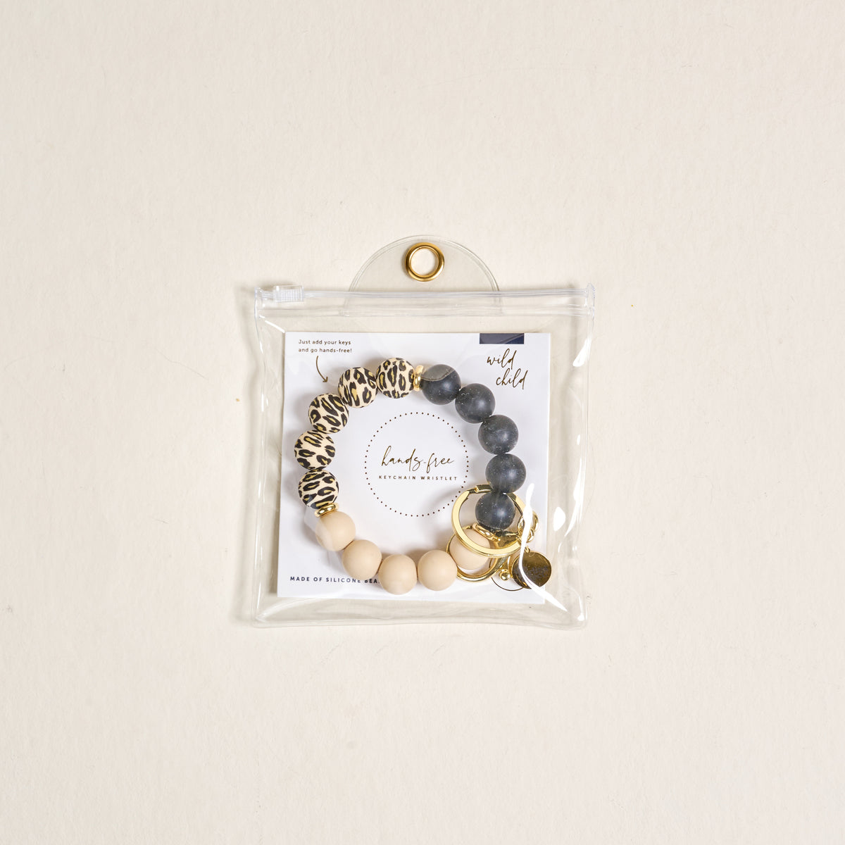 The Wild Child Hands-Free Keychain Wristlet by the-darling-effect features leopard print, dark gray, and beige silicone beads with gold key rings and charms, all in a clear button-closure pouch for chic, hands-free carrying.