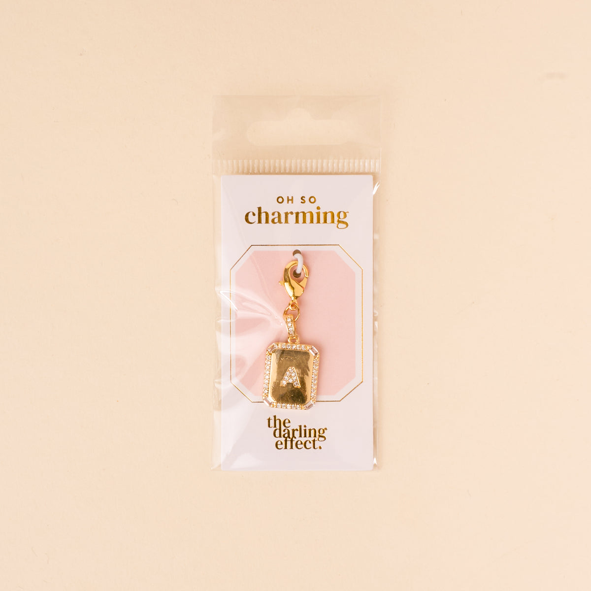 The-darling-effect’s A Jewelry Charm Initial Letter Gold features a gold-plated letter and clasp, attached to an “OH SO charming and the darling effect” card, all in a clear pouch—a perfect personalized jewelry piece.