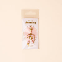 The Darling Effect’s Blushing Bloom Jewelry Charm Gold features gold and pink enamel with a bow and rhinestone, packaged on a light cream OH SO charming card in a clear bag—perfect for your charm bar or jewelry collection.