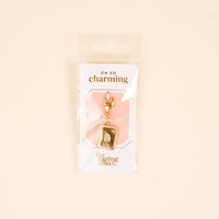 The-darling-effect B Jewelry Charm Initial Letter Gold features a gold-plated "B" charm on a white and peach card with "oh so charming" and "the darling effect," packaged in a clear plastic bag.