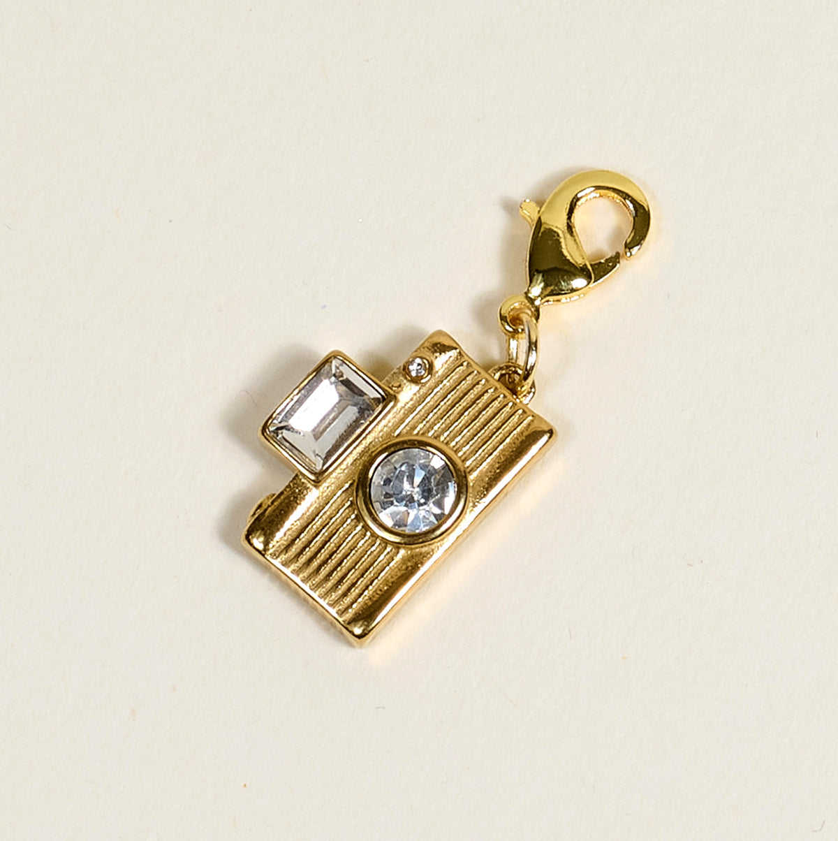 The Darling Effect’s Film Camera Jewelry Charm Gold features a lobster clasp and two clear gemstones—one square, one round—set against a light background, perfect for personalizing your jewelry or charm bar collection.