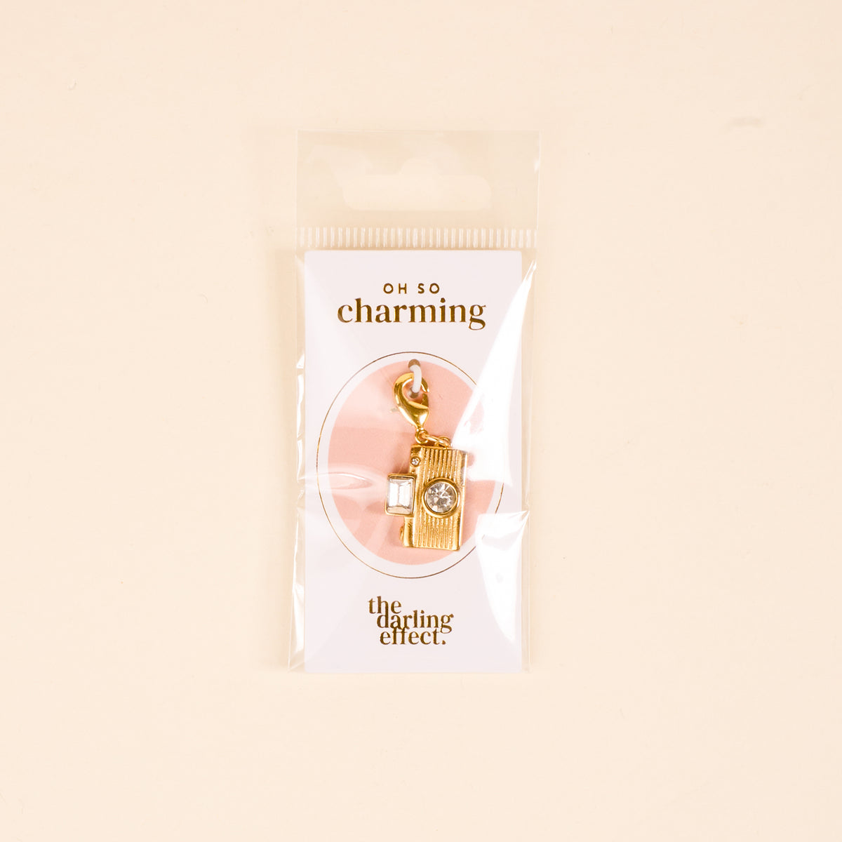 The Darling Effect Film Camera Jewelry Charm Gold features a crystal detail and comes attached to an "OH SO charming" card, packaged in a clear bag—perfect for adding to your personalized jewelry collection.