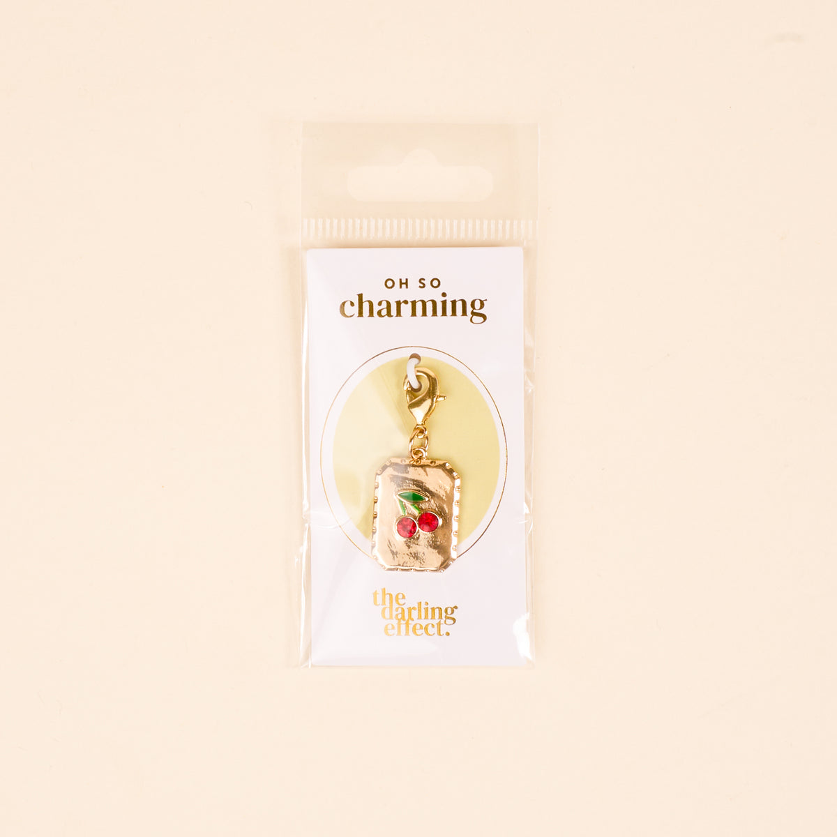 Add a playful touch to your jewelry with The Darling Effect's "A Cherry Moment Jewelry Charm Gold," featuring two red cherries on a stem and lobster clasp. Arrives on a white card with OH SO charming and The Darling Effect branding.