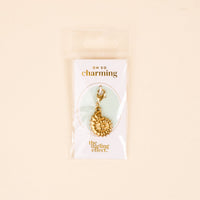 The Darling Effect's Conch Shell Jewelry Charm Gold features a clasp and comes on a white card reading "OH SO charming" and The Darling Effect, packaged in a clear bag with a light beige background—ideal for your charm bar or unique jewelry.