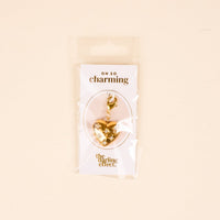 The Diamond Heart Jewelry Charm Gold by The Darling Effect features a gold, heart-shaped design with a clasp, packaged on an "OH SO charming" card—perfect for adding a meaningful touch to your charm bar.