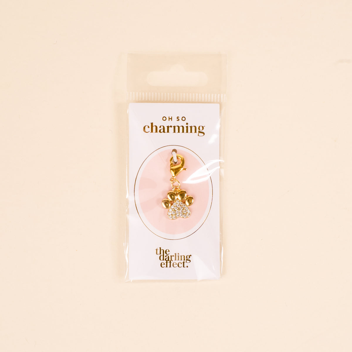 The Darling Effect's Dazzled Paw Print Jewelry Charm Gold features a rhinestone-studded paw design on an OH SO charming card, packaged in a clear sleeve—perfect for adding sparkle to any charm bar collection.