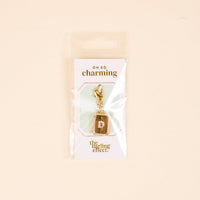 The D Jewelry Charm Initial Letter Gold by the-darling-effect is a gold-plated rectangular charm with a sparkling center detail, packaged on a card reading "OH SO charming and the darling effect"—ideal for initial letter jewelry fans.