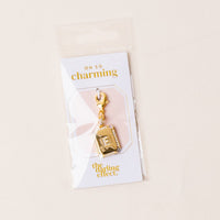 The-darling-effect’s E Jewelry Charm Initial Letter Gold features a gold-plated brass rectangular pendant engraved with “E,” attached to an Oh So Charming card and packaged in a clear plastic sleeve—ideal for personalized jewelry lovers.
