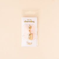 The E Jewelry Charm Initial Letter Gold by the-darling-effect features a gold-plated brass book-shaped charm with silver accents and a lobster clasp, presented on a white "OH SO charming" card in clear plastic packaging.