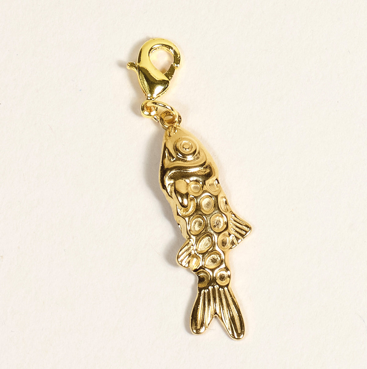 The Darling Effect Fish Jewelry Charm Gold features a textured, scale-like pattern and a lobster clasp, ideal for charm bars or layering necklaces. Shown against a plain light background.