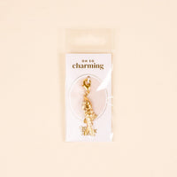 The Darling Effect Fish Jewelry Charm Gold features intricate detailing, comes attached to an "Oh So Charming" card, and is packaged in a clear sleeve against a light beige background—perfect for your charm bar.