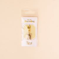 The-darling-effect’s G Jewelry Charm Initial Letter Gold features a gold-plated brass charm with rhinestones and a rectangular frame, hanging from a lobster clasp on an “Oh So Charming” card—perfect for lovers of personalized jewelry.