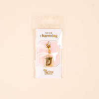 The-darling-effect J Jewelry Charm Initial Letter Gold features a gold-plated brass "J" with a glitter border, clasp, and is displayed on a branded card in clear packaging—perfect personalized jewelry on a cute pink-and-white background.