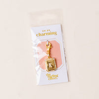 The K Jewelry Charm Initial Letter Gold by the-darling-effect features gold plating and rhinestones, attached to a lobster clasp. It comes in a clear package labeled "oh so charming" with a light neutral background for a personalized touch.
