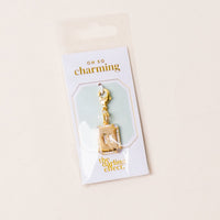 The-darling-effect’s M Jewelry Charm Initial Letter Gold features a gold-plated brass “M” with rhinestones, displayed in clear packaging labeled OH SO charming. Ideal for personalized jewelry or as an initial letter charm. Background is light and neutral.