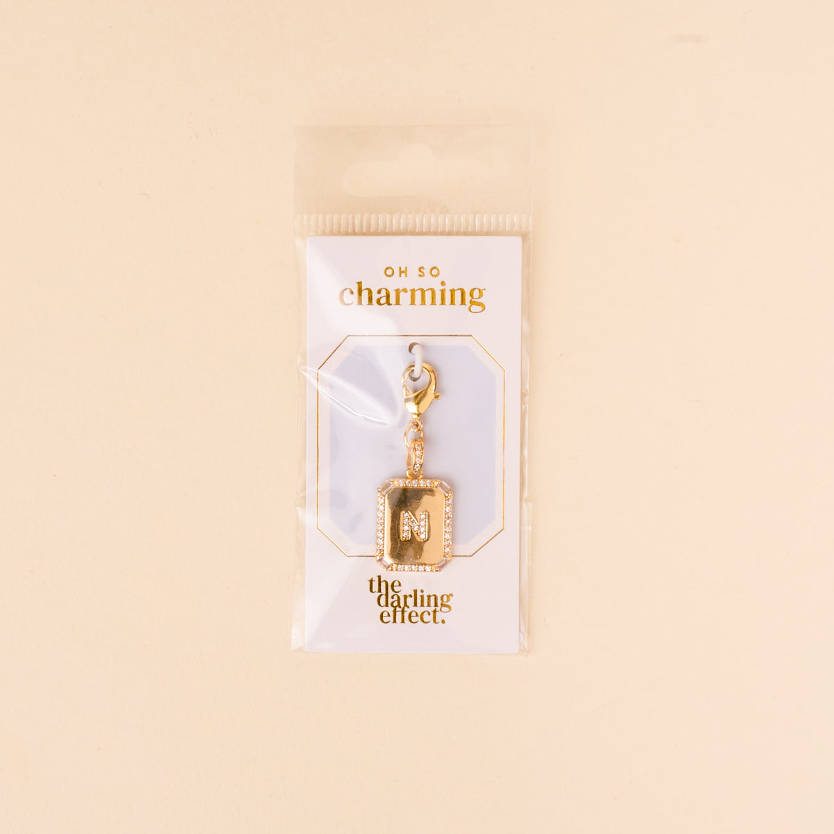 The-darling-effect N Jewelry Charm Initial Letter Gold features a gold-plated brass M encrusted with small gems and a lobster clasp, displayed on an OH SO charming card in clear packaging.