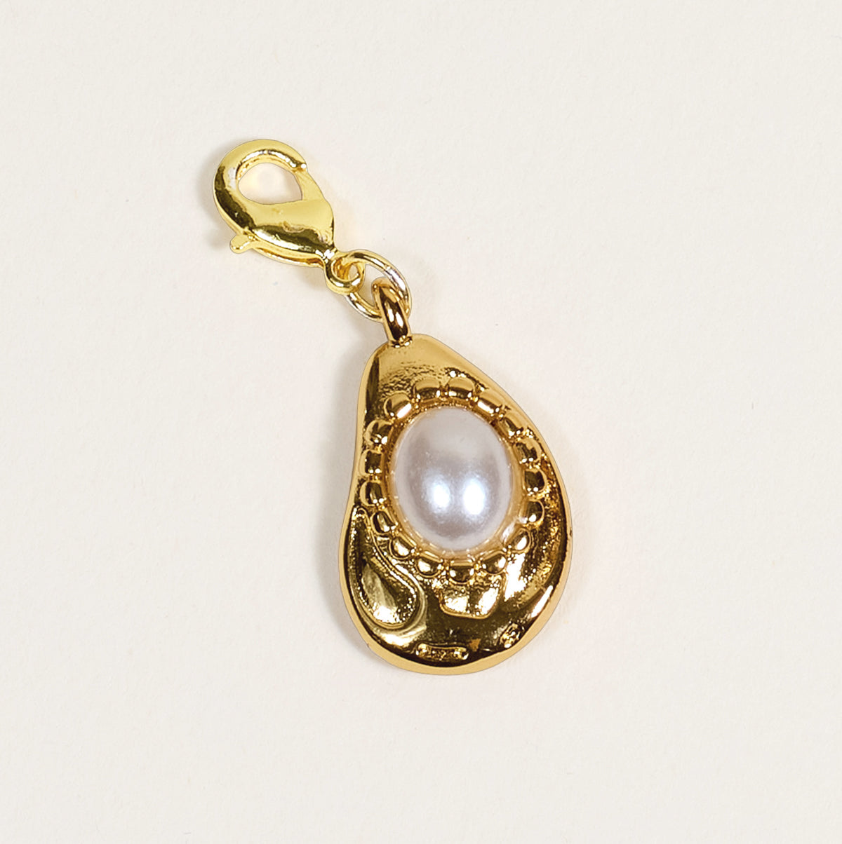 The Darling Effect's Oyster Jewelry Charm Gold features a lobster clasp and teardrop-shaped frame with intricate detailing around a central white pearl, shown on a plain light background—perfect for your charm bar.