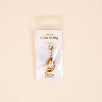 The Darling Effect's Oyster Jewelry Charm Gold keychain features a pearl charm and comes attached to an “OH SO charming & the darling effect” card, all packaged in a clear plastic bag.