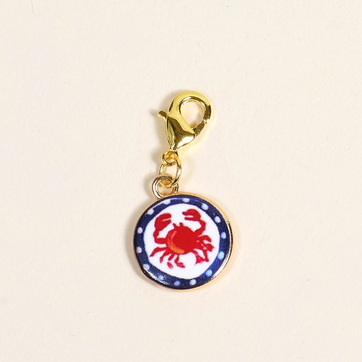 The Darling Effect Painted Crab Jewelry Charm Gold features a round charm with a red crab on white, blue dotted border, and gold lobster clasp—perfect for adding coastal flair to your charm bar or bracelet.