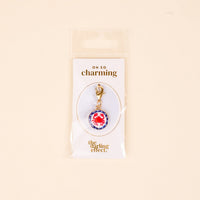 The Darling Effect Painted Crab Jewelry Charm Gold features a red crab on a blue and white background with a gold clasp, perfect for your charm bar. Packaged on a white Oh So Charming card, it’s a delightful jewelry addition.