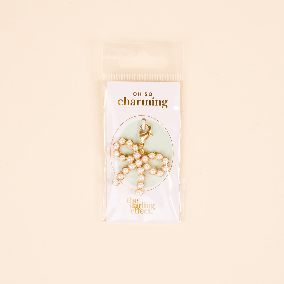 The Darling Effect Pretty in Pearl Bow Jewelry Charm Gold features pearls and a clasp, ideal for charm jewelry lovers. Presented on an OH SO charming card with The Darling Effect logo, in clear packaging.