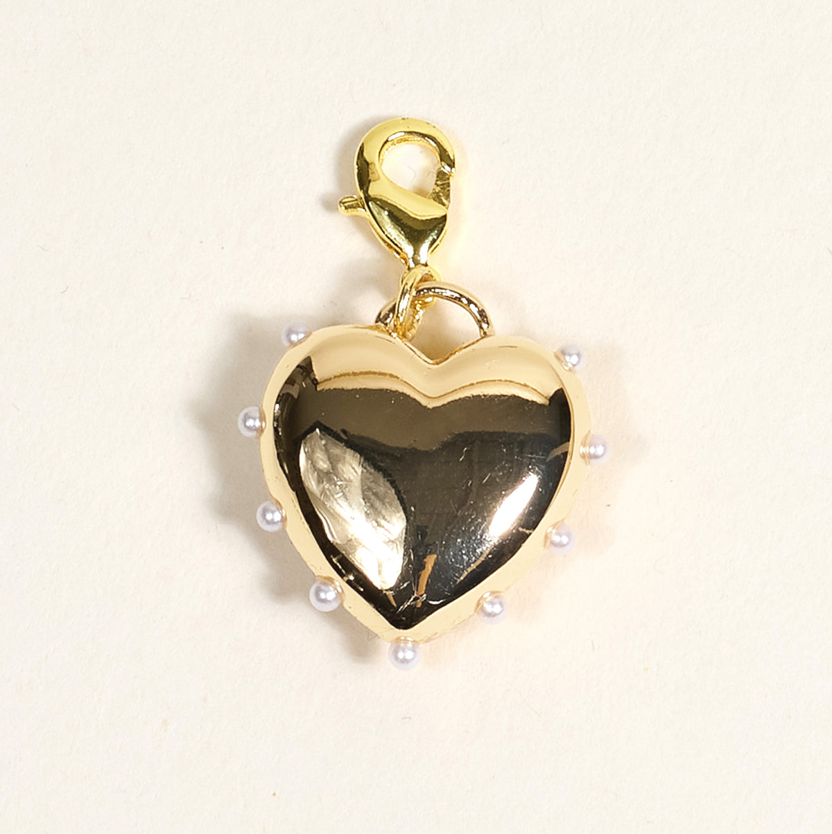 The Darling Effect’s Pearl Lined Heart Jewelry Charm Gold features a gold heart shape, small white pearls along the edge, and a lobster clasp—perfect for charm jewelry or your own charm bar. Photographed on a light beige background.