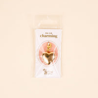 The Darling Effect’s Pearl Lined Heart Jewelry Charm Gold features a lobster clasp, ideal for layering on your charm bar. It comes on a white and pink OH SO charming card in a clear bag against a pale beige background.