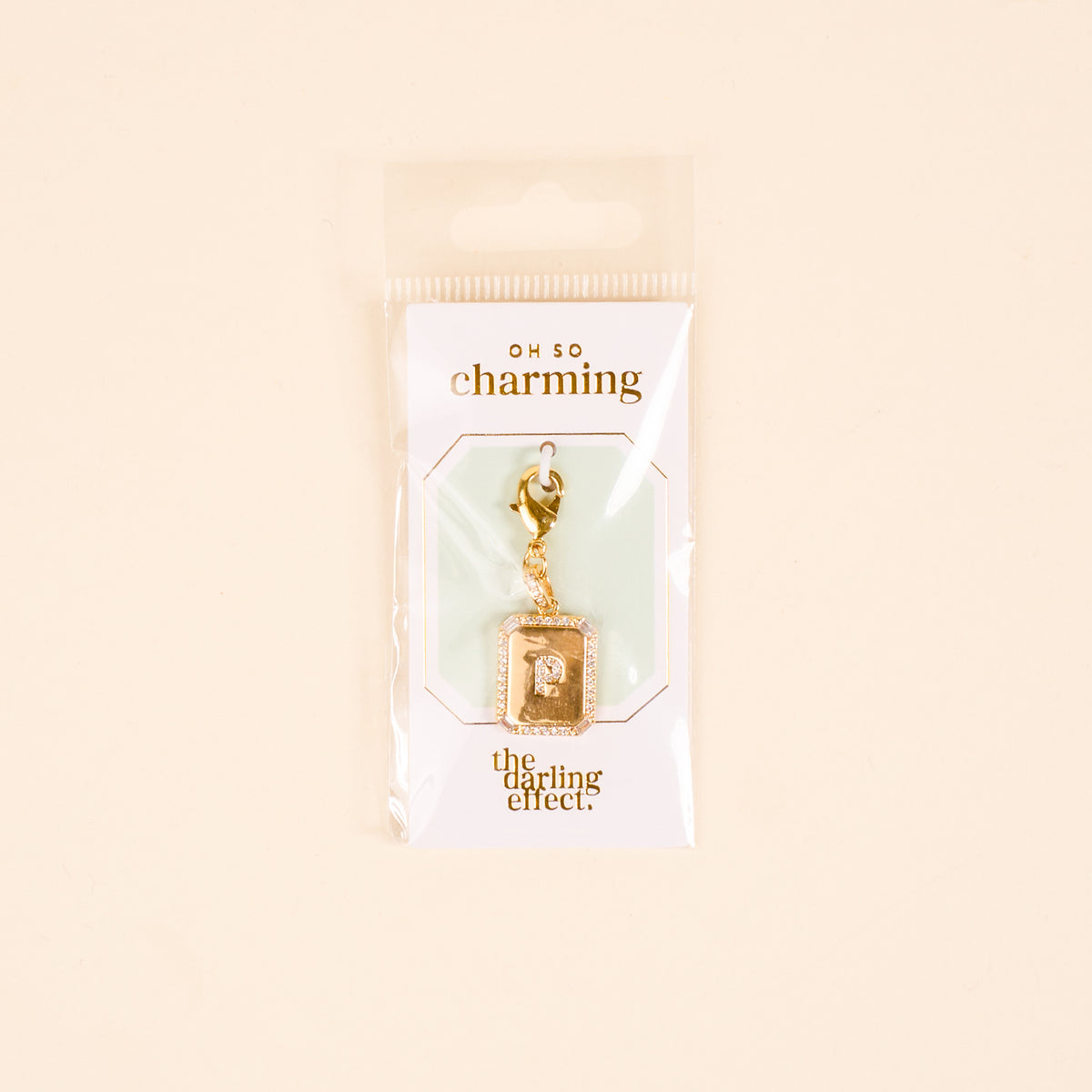 The P Jewelry Charm Initial Letter Gold by the-darling-effect is a gold-plated brass lock-shaped charm on a white card with gold "OH SO charming" and "the darling effect" text, packaged in a clear bag—ideal for personalized jewelry.