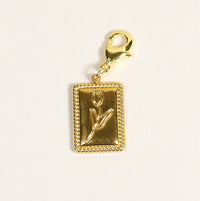 The Darling Effect's Tulip Time Jewelry Charm Gold features a raised tulip on a golden rectangular bar with a gold lobster clasp—ideal for adding a meaningful touch to your favorite charm jewelry.