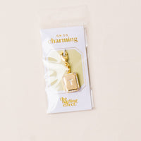 The T Jewelry Charm Initial Letter Gold by the-darling-effect features a gold-plated brass charm with a beveled frame, diamond accents, and a central white T. Packaged with OH SO charming and the darling effect logos.