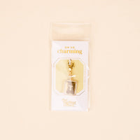The-darling-effect T Jewelry Charm Initial Letter Gold: a gold-plated brass charm keychain featuring the letter T on gray, packaged on a white card with “OH SO charming” and “the darling effect” in a clear sleeve.