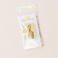 The-darling-effect's V Jewelry Charm Initial Letter Gold features a gold-plated initial with a lobster clasp, attached to an "OH SO charming" card and packaged in a clear sleeve—perfect for personalizing your jewelry.