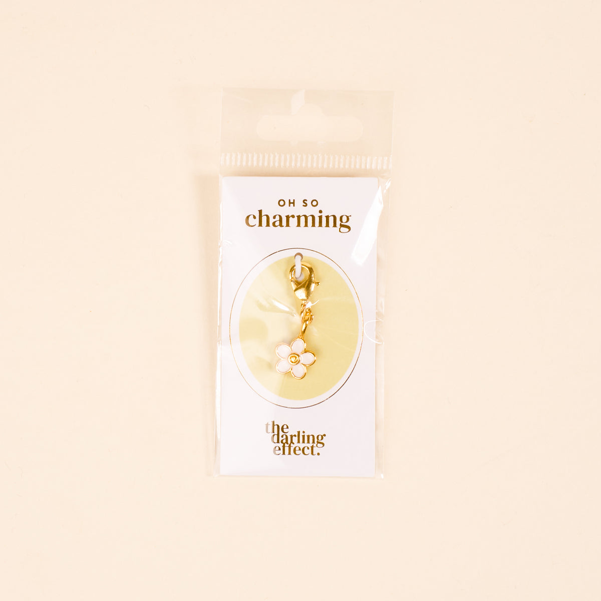 The-darling-effect White Flower Jewelry Charm Gold features a gold-tone charm with a white flower and yellow center, hanging from a clasp—ideal for your charm bar. It comes on an "OH SO charming" card.