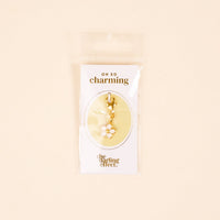 The-darling-effect White Flower Jewelry Charm Gold features a gold-tone charm with a white flower and yellow center, hanging from a clasp—ideal for your charm bar. It comes on an "OH SO charming" card.