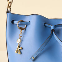 A close-up of a blue leather bucket bag features the-darling-effect's K Bubble Letter Keychain Bag Charm and a darling effect tag.