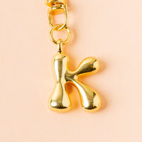 The K Bubble Letter Keychain Bag Charm by the-darling-effect features a shiny gold "K" bubble letter, perfect as a personalized charm for your keys or bag.