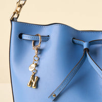 Close-up of a light blue leather handbag with drawstring closure, gold hardware, and the-darling-effect’s N Bubble Letter Keychain Bag Charm featuring a round charm and the letter N attached to the strap.