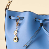 Close-up of a blue leather drawstring bag with a gold chain strap, featuring the-darling-effect’s O Bubble Letter Keychain Bag Charm.